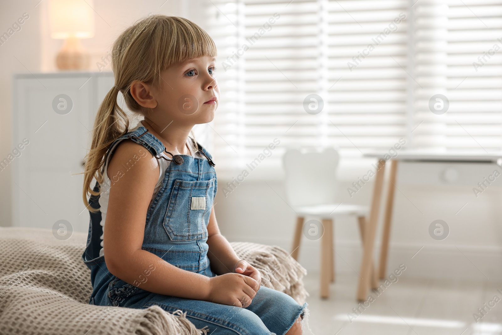 Photo of Orphanage concept. Sad little girl sitting on bed indoors, space for text