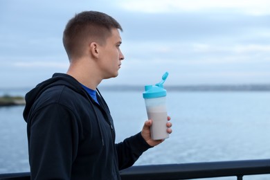 Photo of Athletic man with shaker of protein drink outdoors. Space for text