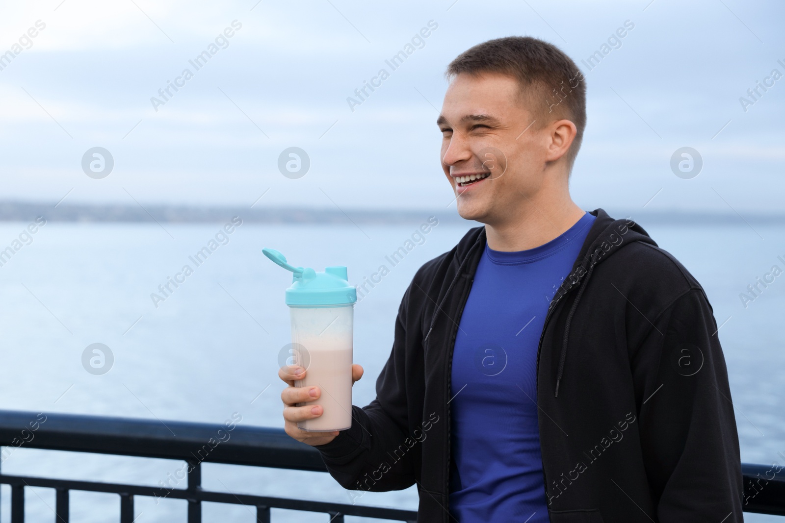 Photo of Smiling man with shaker of protein drink outdoors. Space for text