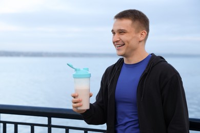 Smiling man with shaker of protein drink outdoors. Space for text