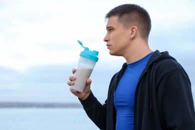 Photo of Athletic man with shaker of protein drink outdoors. Space for text