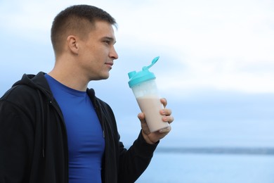 Photo of Athletic man with shaker of protein drink outdoors. Space for text