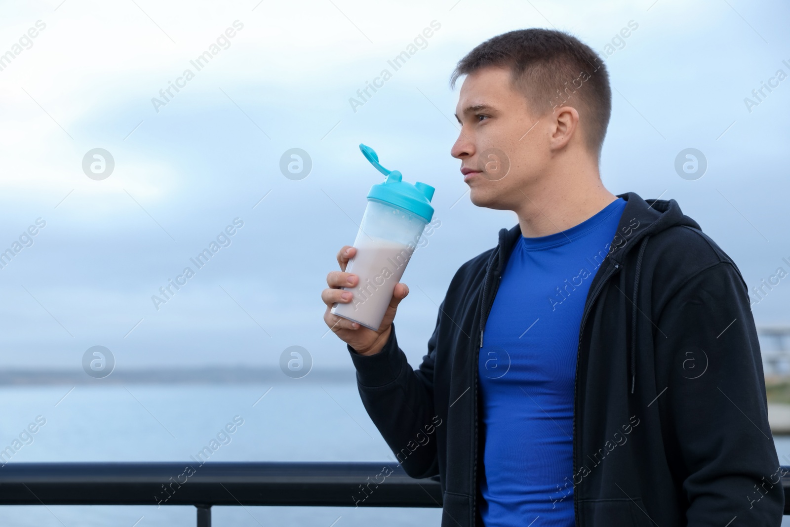 Photo of Athletic man with shaker of protein drink outdoors. Space for text