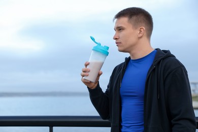 Photo of Athletic man with shaker of protein drink outdoors. Space for text