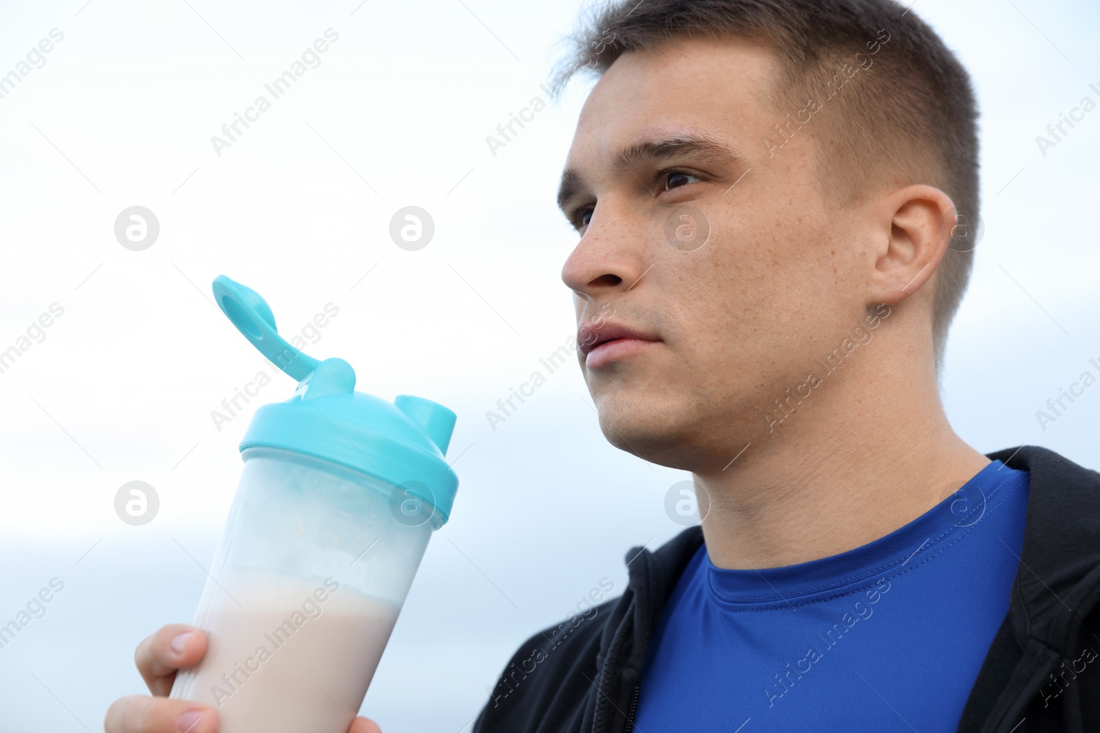 Photo of Athletic man with shaker of protein drink outdoors, closeup