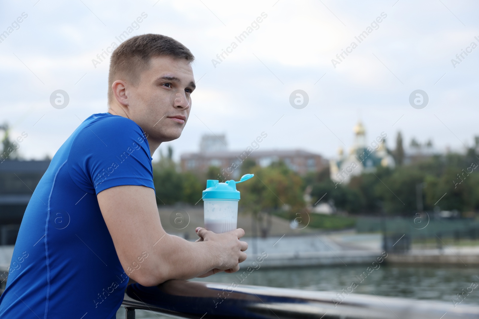 Photo of Athletic man with shaker of protein drink outdoors. Space for text