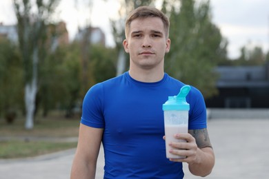 Athletic man with shaker of protein drink outdoors