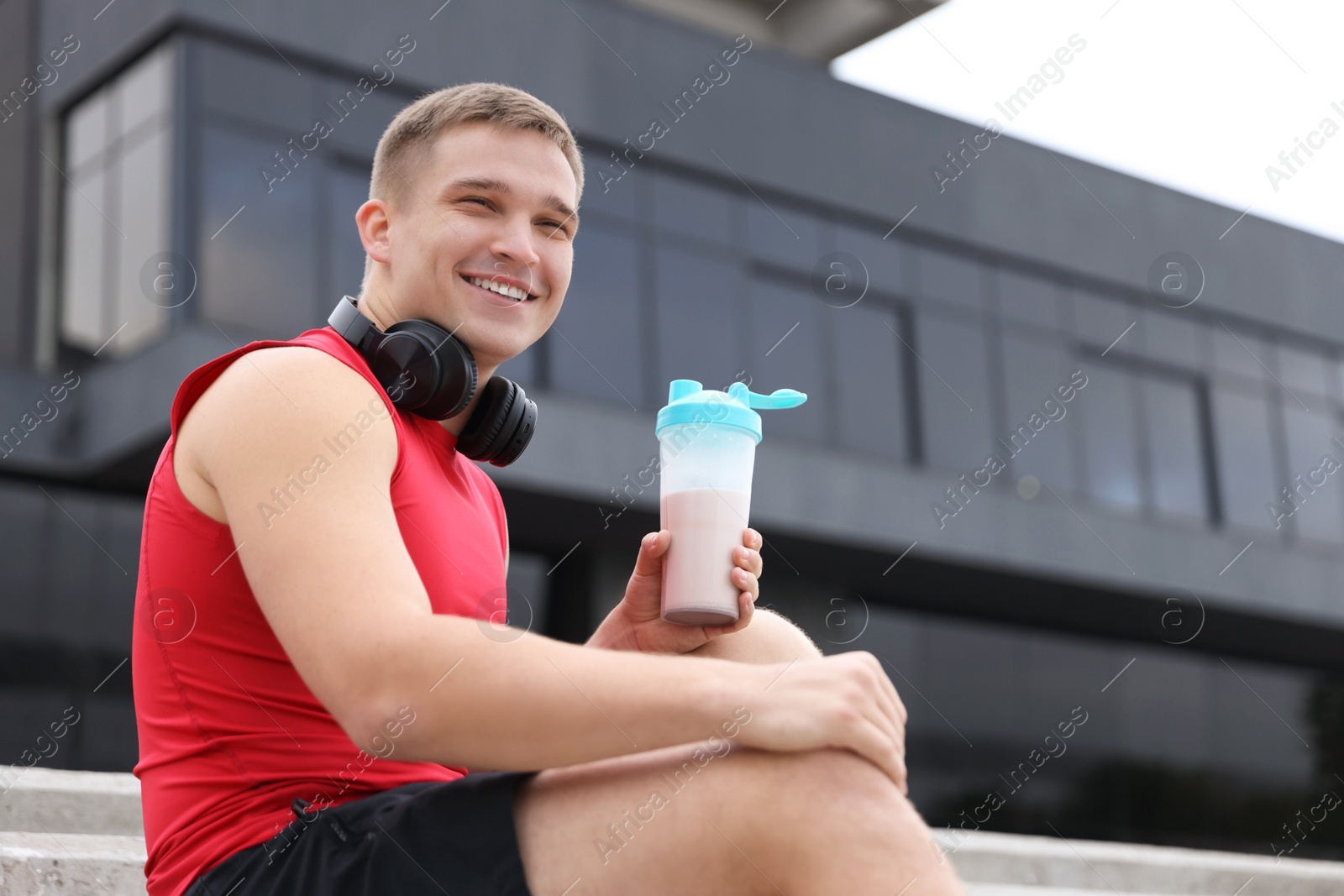 Photo of Smiling man with shaker of protein drink outdoors, low angle view