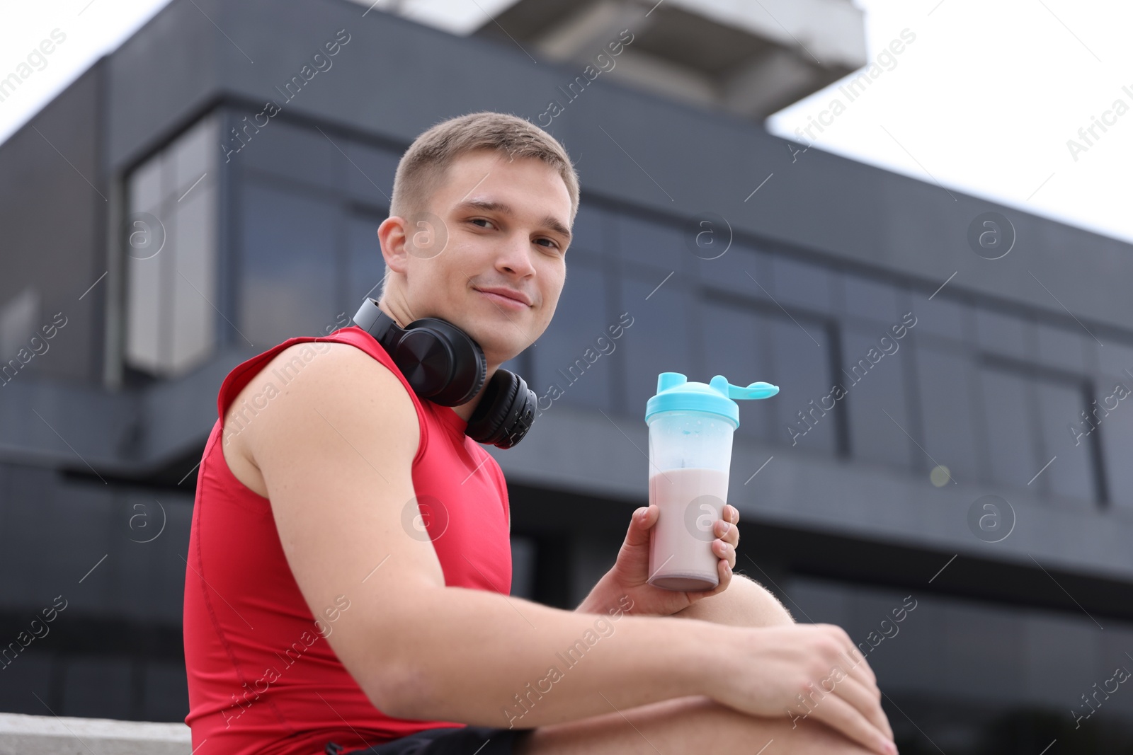 Photo of Athletic man with shaker of protein drink outdoors, low angle view