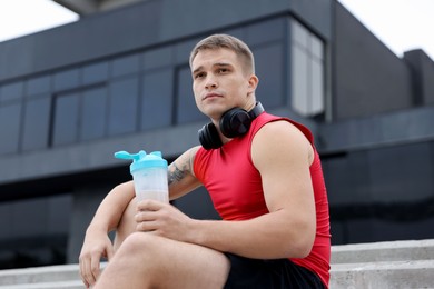 Athletic man with shaker of protein drink outdoors, low angle view