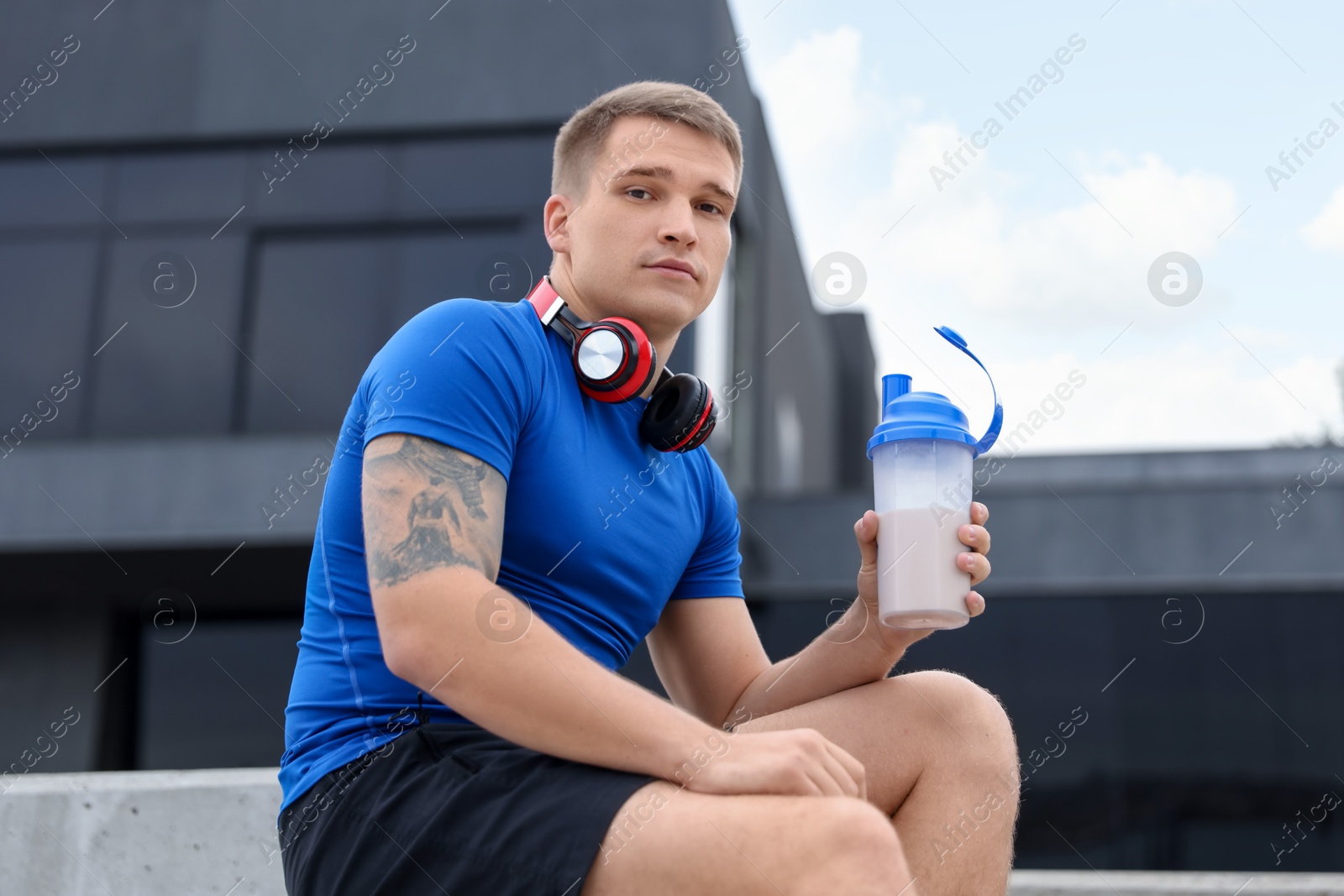 Photo of Athletic man with shaker of protein drink outdoors, low angle view