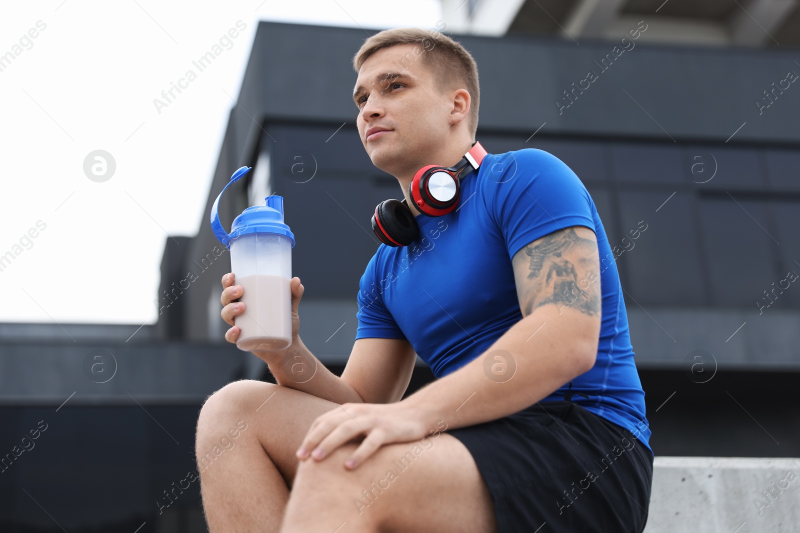 Photo of Athletic man with shaker of protein drink outdoors, low angle view