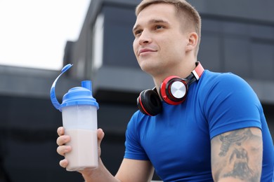 Athletic man with shaker of protein drink outdoors