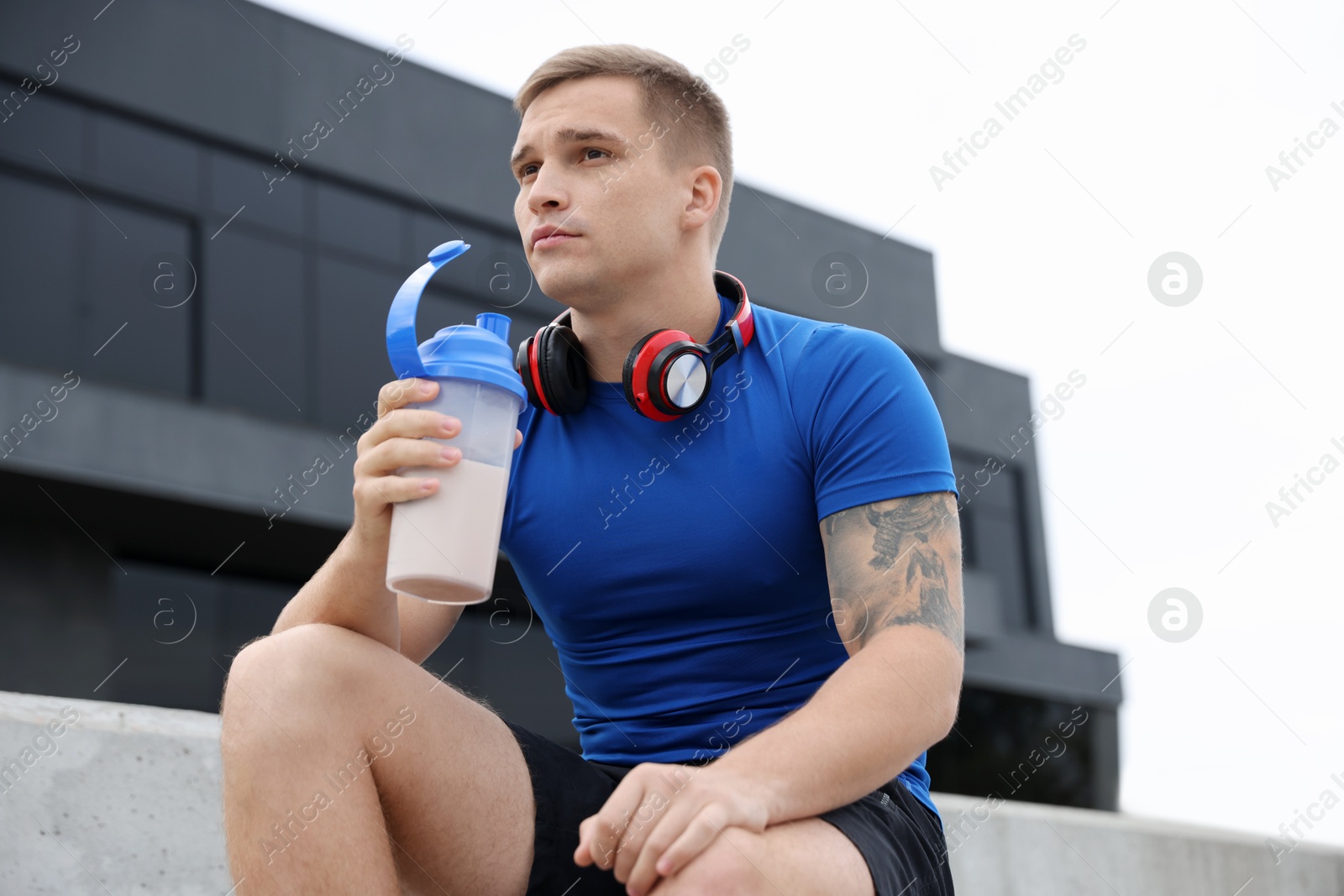 Photo of Athletic man with shaker of protein drink outdoors, low angle view