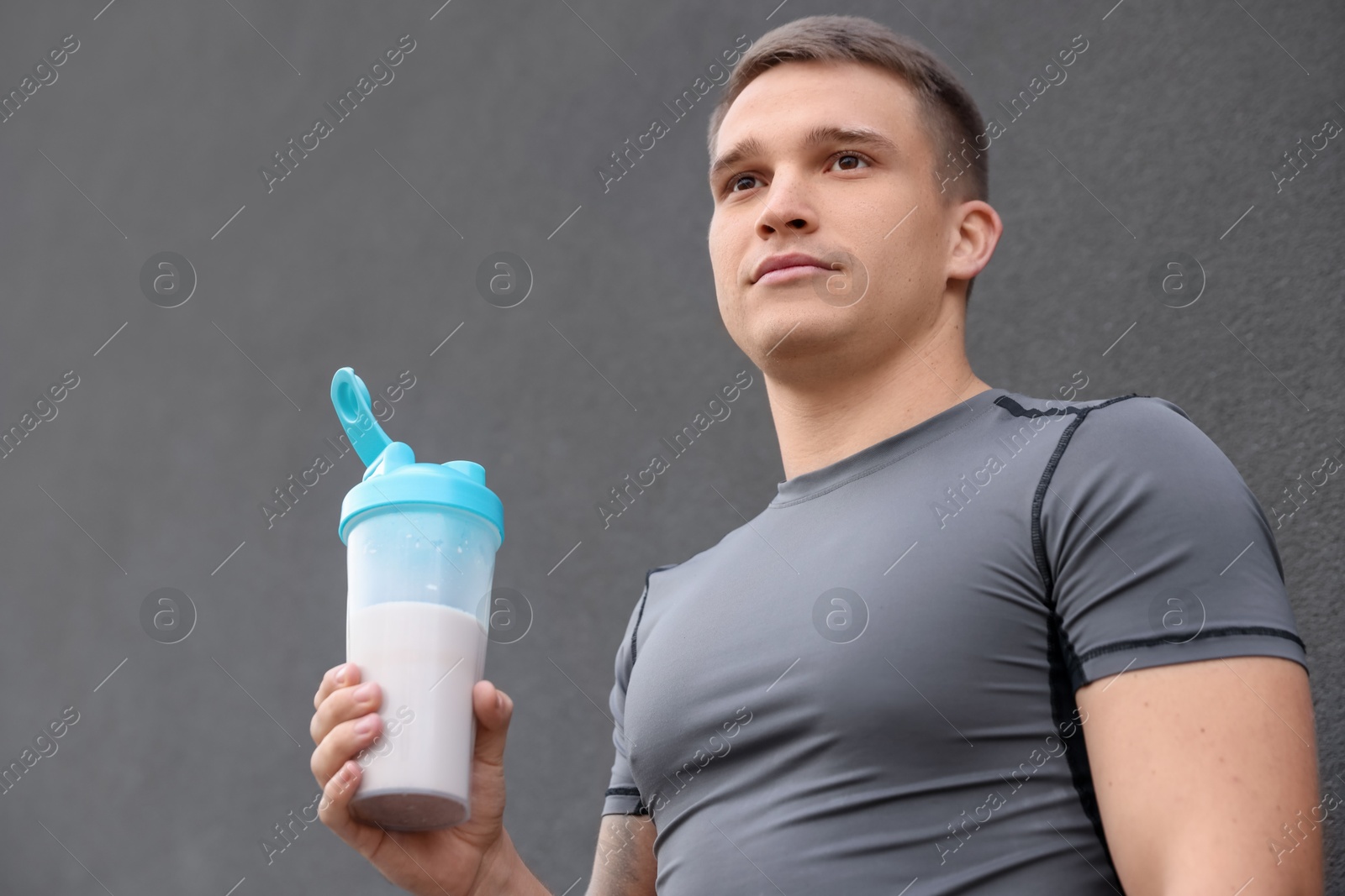 Photo of Athletic man with shaker of protein drink near grey wall, low angle view