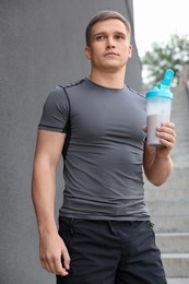 Photo of Athletic man with shaker of protein drink near grey wall outdoors