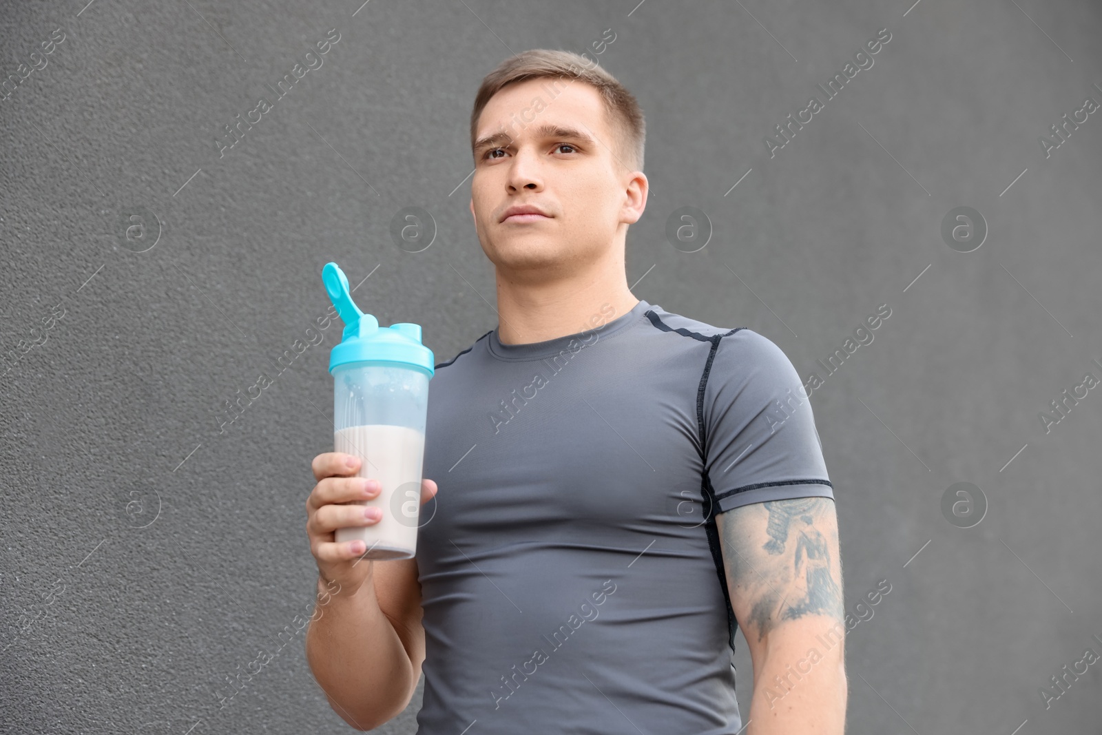 Photo of Athletic man with shaker of protein drink near grey wall