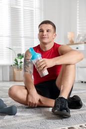 Photo of Athletic man with shaker of protein drink sitting on carpet at home