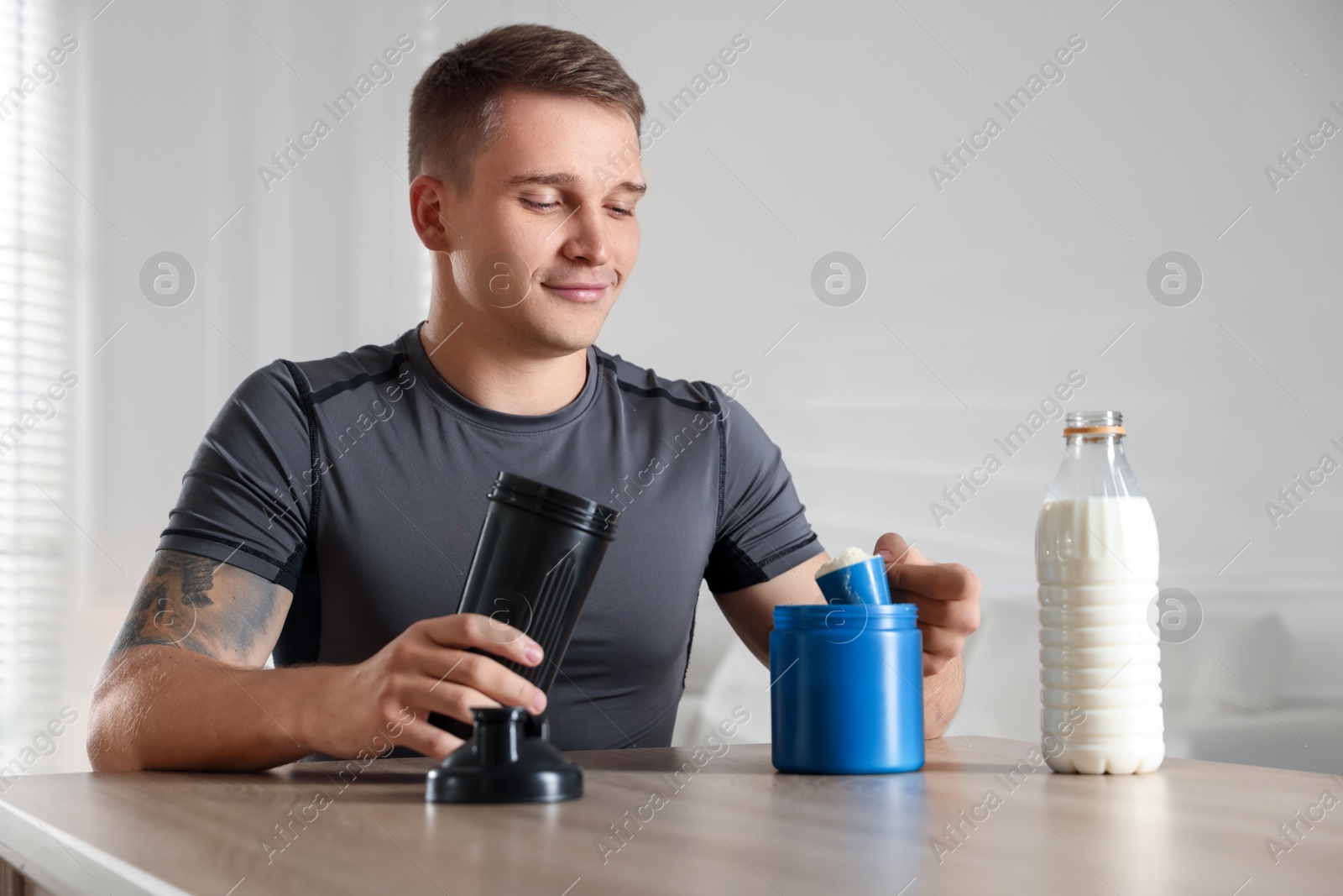 Photo of Making protein cocktail. Man with scoop of powder and shaker at wooden table