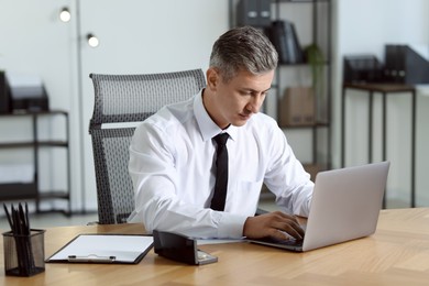 Photo of Businessman working on laptop at table in office