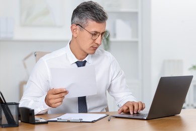 Photo of Businessman working on laptop at table in office