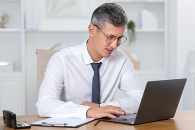 Photo of Businessman working on laptop at table in office