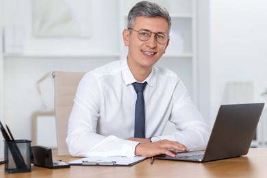 Photo of Businessman working on laptop at table in office