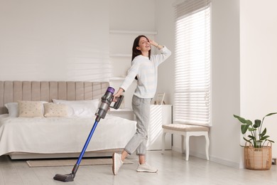 Photo of Smiling young woman cleaning floor with cordless vacuum cleaner in bedroom