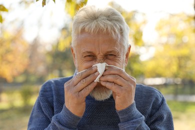 Senior man with tissue blowing runny nose in park