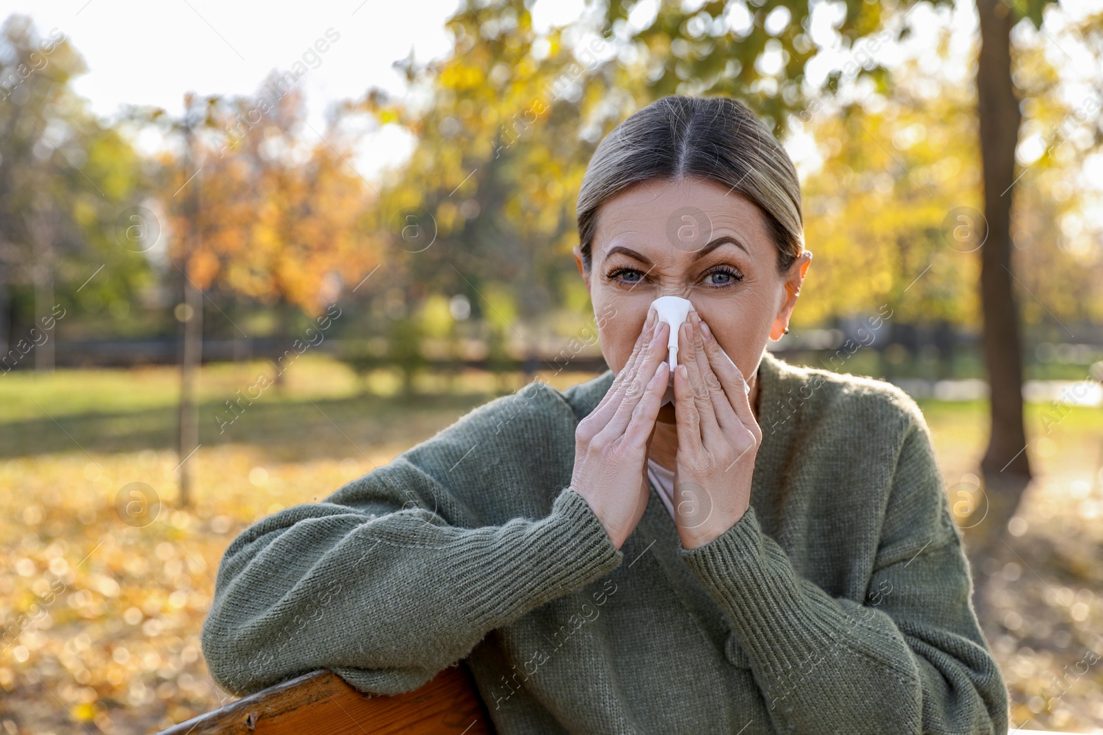 Photo of Woman with tissue blowing runny nose in park