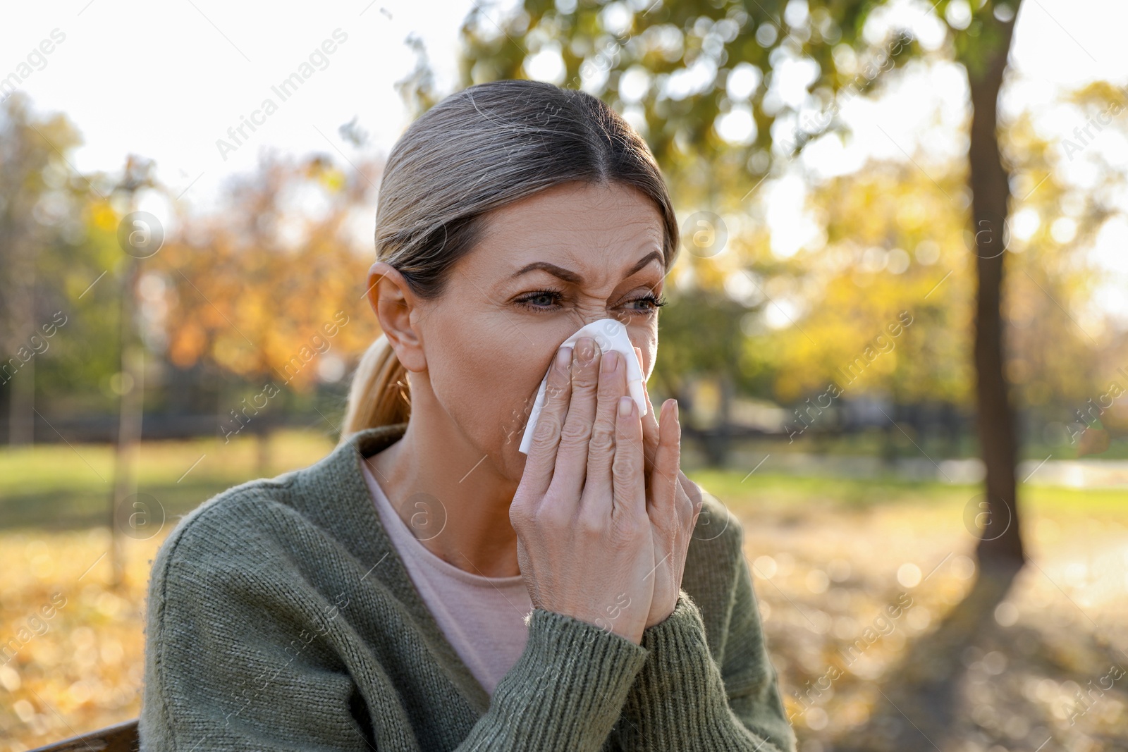 Photo of Woman with tissue blowing runny nose in park