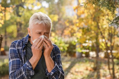 Senior man with runny nose in park, space for text