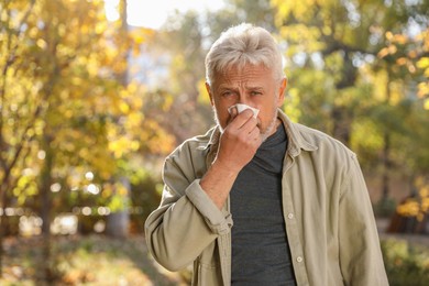 Senior man with runny nose in park, space for text