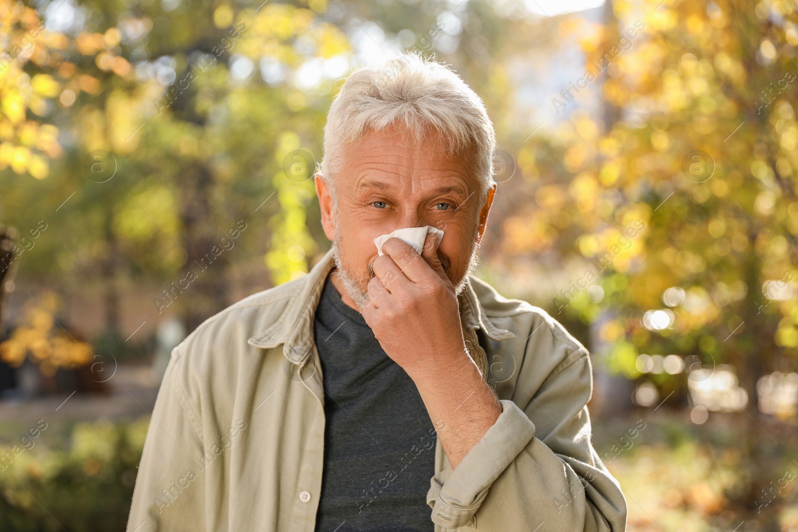 Photo of Senior man with tissue blowing runny nose in park