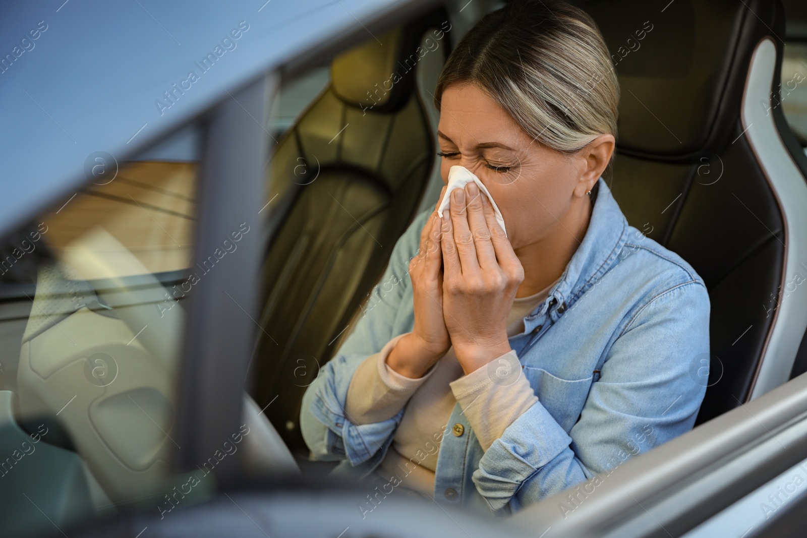 Photo of Woman with tissue blowing runny nose in car