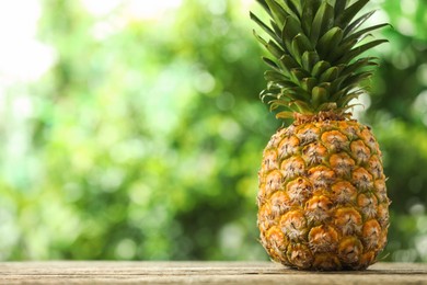 Photo of Fresh ripe pineapple on wooden table against blurred background, space for text