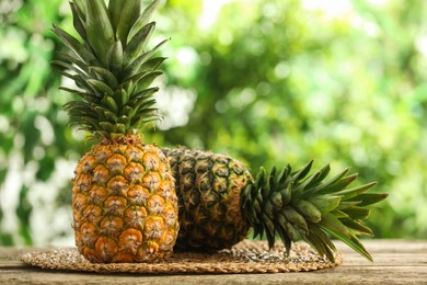 Photo of Fresh ripe pineapples on wooden table against blurred background, space for text