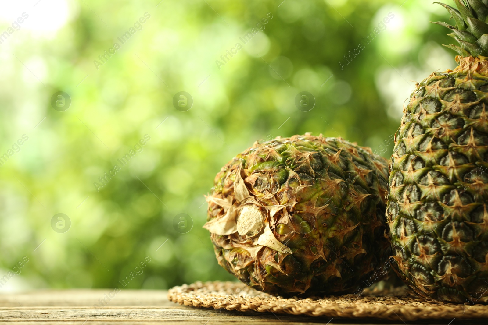 Photo of Fresh ripe pineapples on wooden table against blurred background, closeup. Space for text