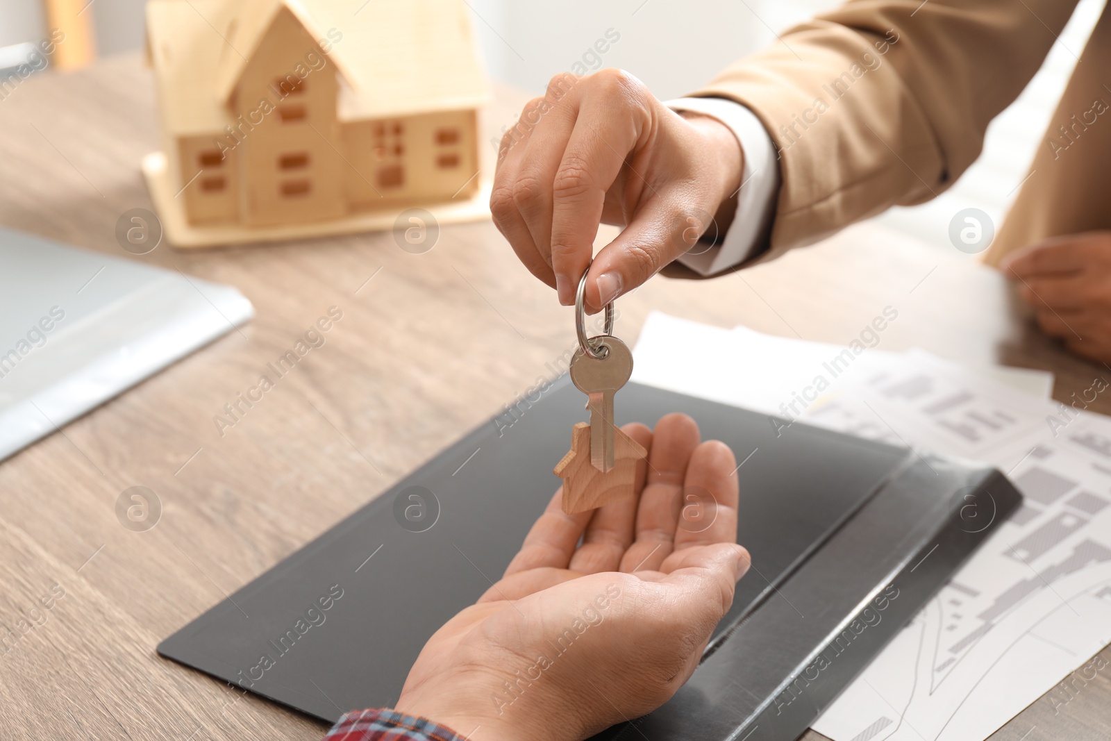 Photo of Real estate agent giving house key to new owner at wooden table, closeup