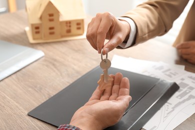 Photo of Real estate agent giving house key to new owner at wooden table, closeup