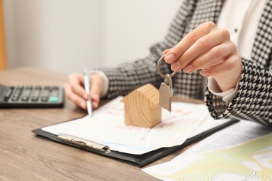 Real estate agent with house key working at wooden table, closeup