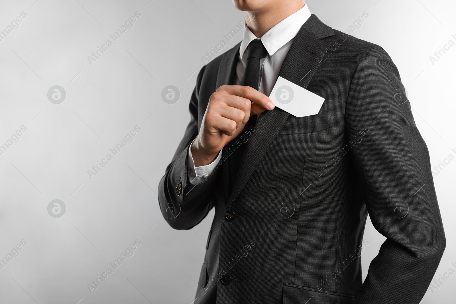 Photo of Man taking blank business card from pocket of his jacket on grey background, closeup. Mockup for design