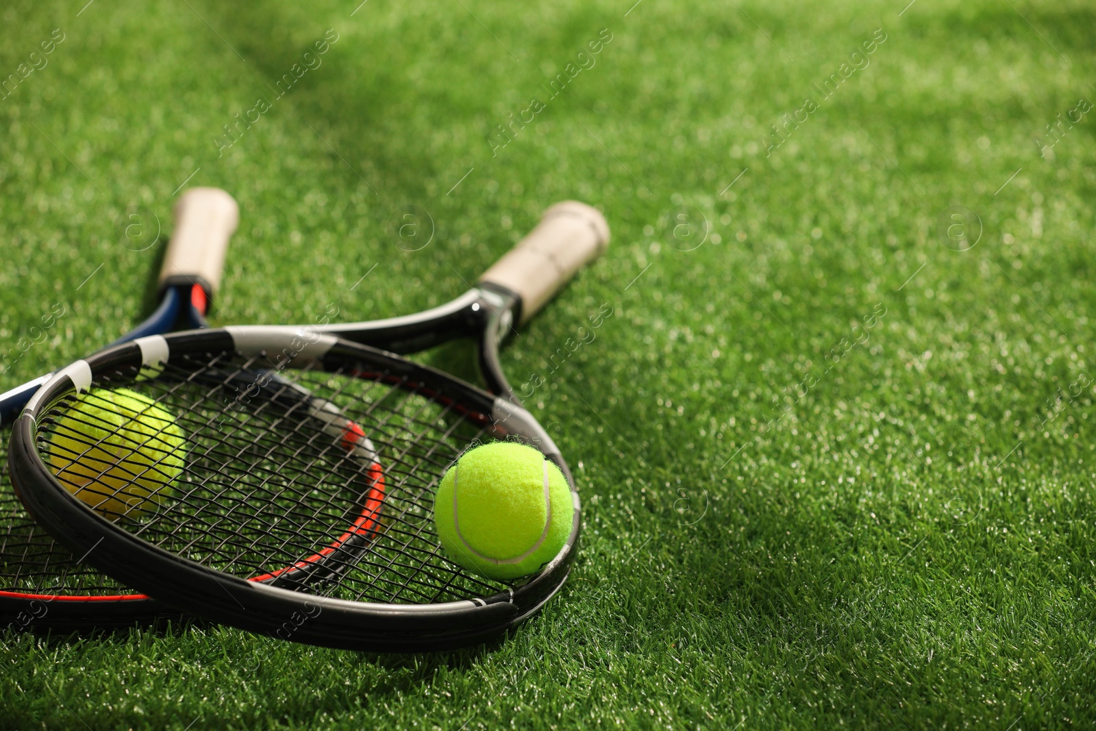 Photo of Tennis rackets and balls on green artificial grass, space for text