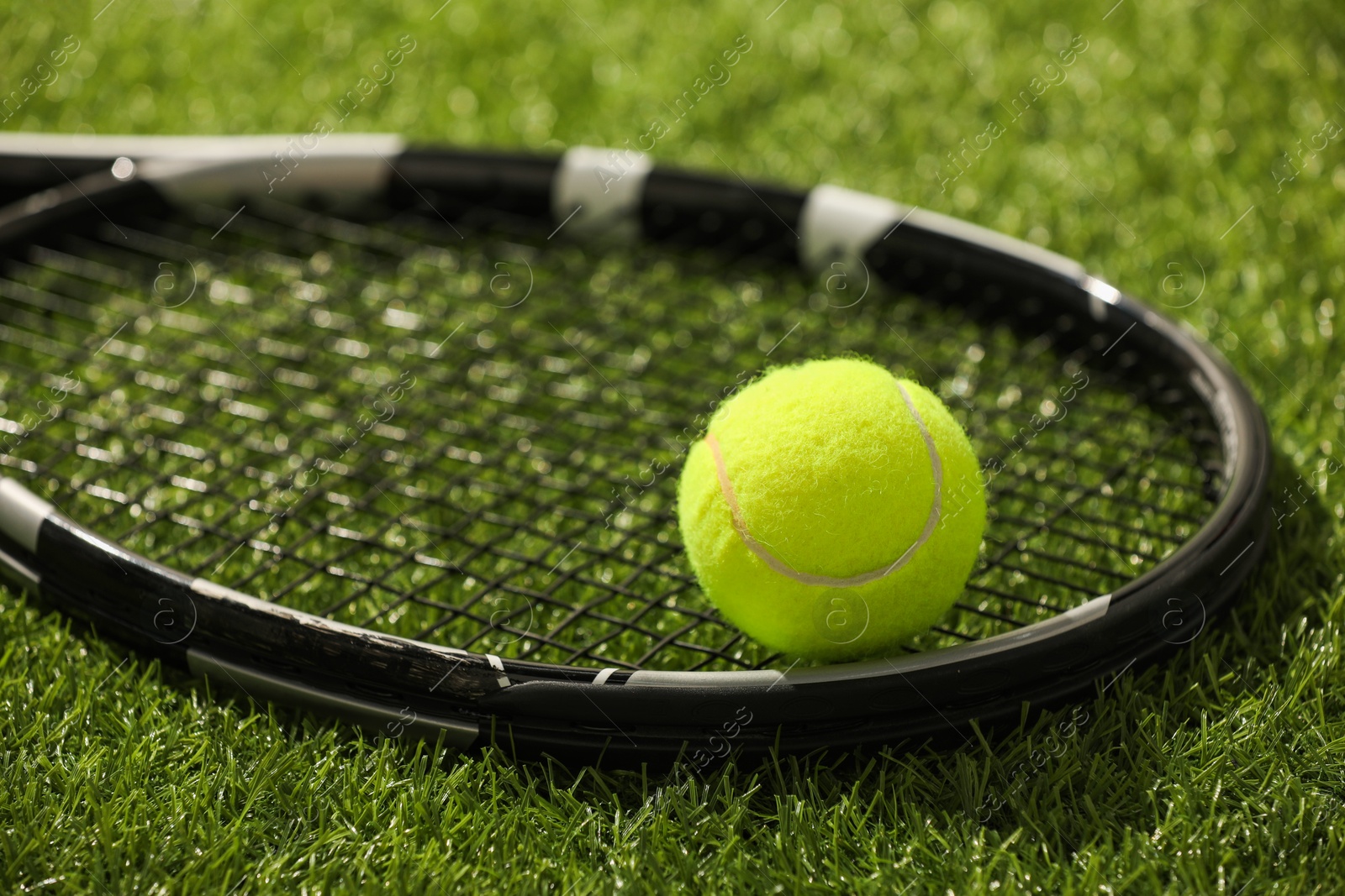 Photo of Tennis racket and ball on green artificial grass, closeup