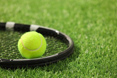 Photo of Tennis racket and ball on green artificial grass, closeup. Space for text