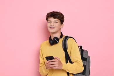 Photo of Teenage boy with headphones, smartphone and backpack on pink background