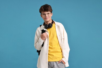 Photo of Teenage boy with headphones and backpack on light blue background