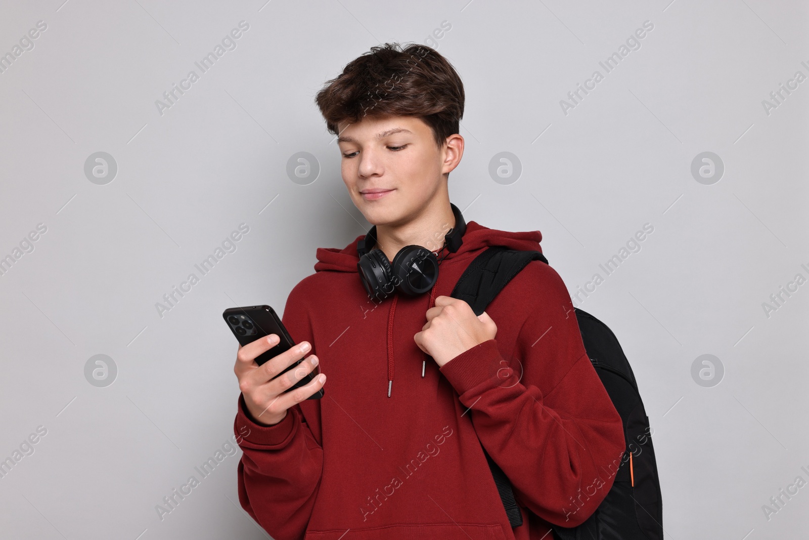 Photo of Teenage boy with headphones, smartphone and backpack on light grey background