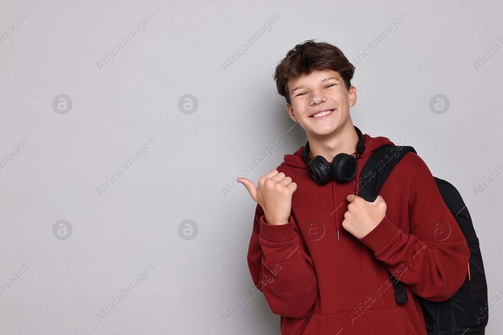 Photo of Happy teenage boy with headphones and backpack on light grey background, space for text