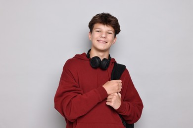 Photo of Happy teenage boy with headphones and backpack on light grey background